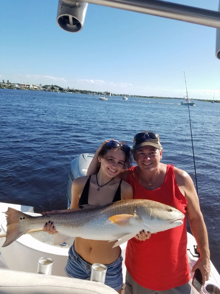 a father and daughter holding a redfish on a boat in new smyrna beach, fl