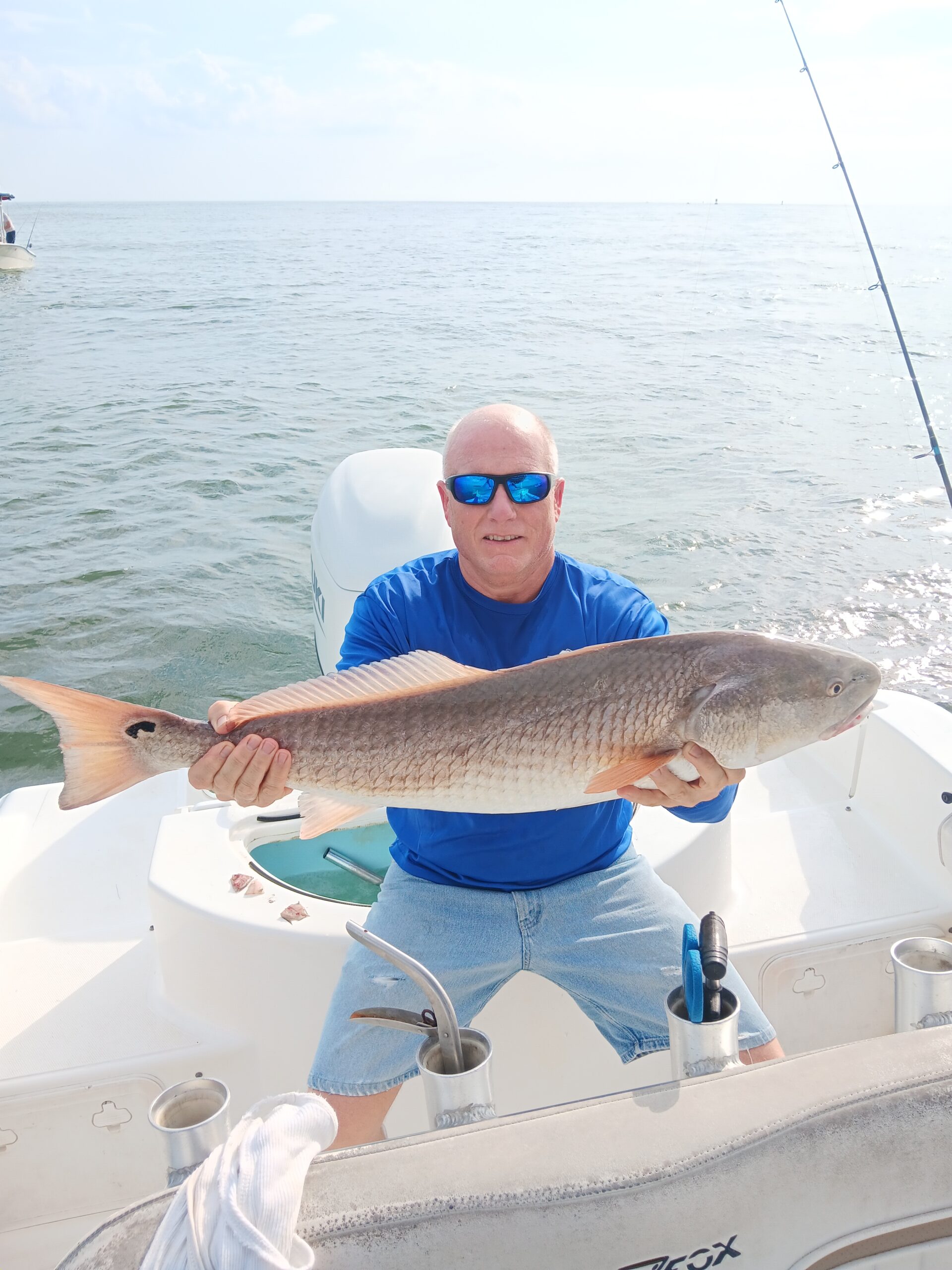 a guy holding a red fish on a boat in new smyrna beach fl