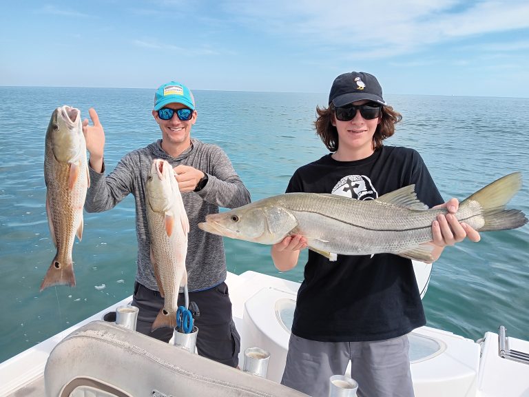 a guy and a boy holding a redfish and snook on a boat in new smyrna beach, fl