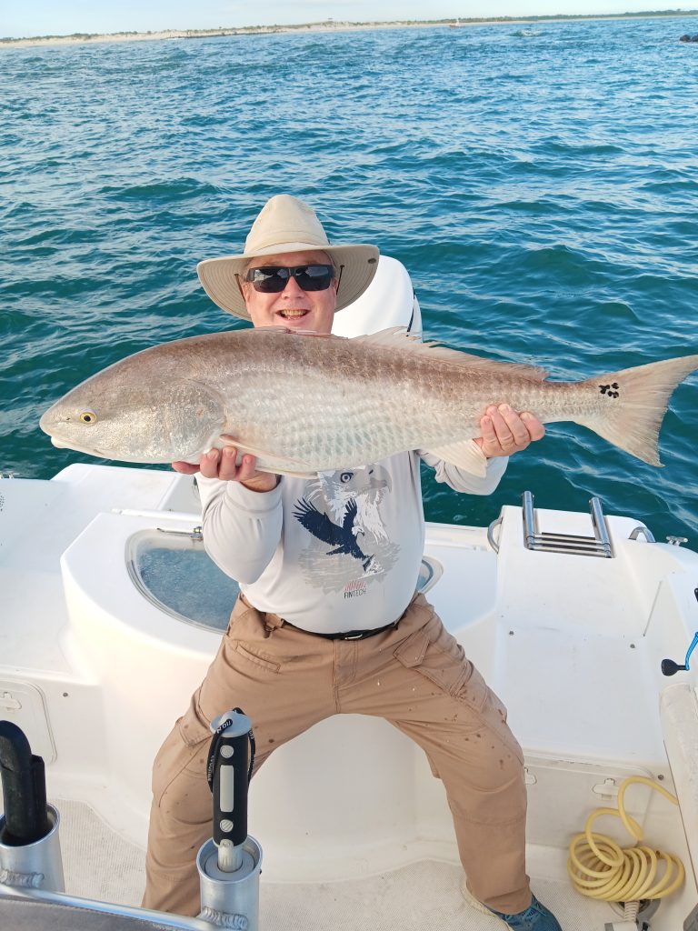 a guy holding a redfish on a boat in new smyrna beach, fl