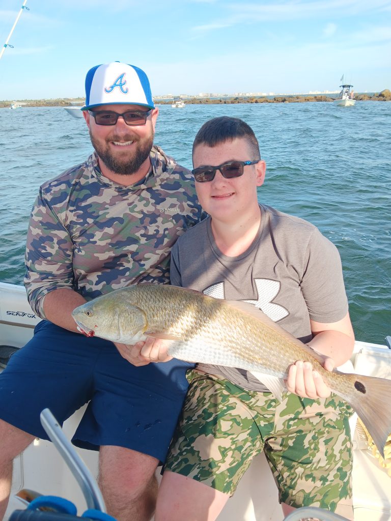 a guy holding a redfish on a boat in new smyrna beach, fl