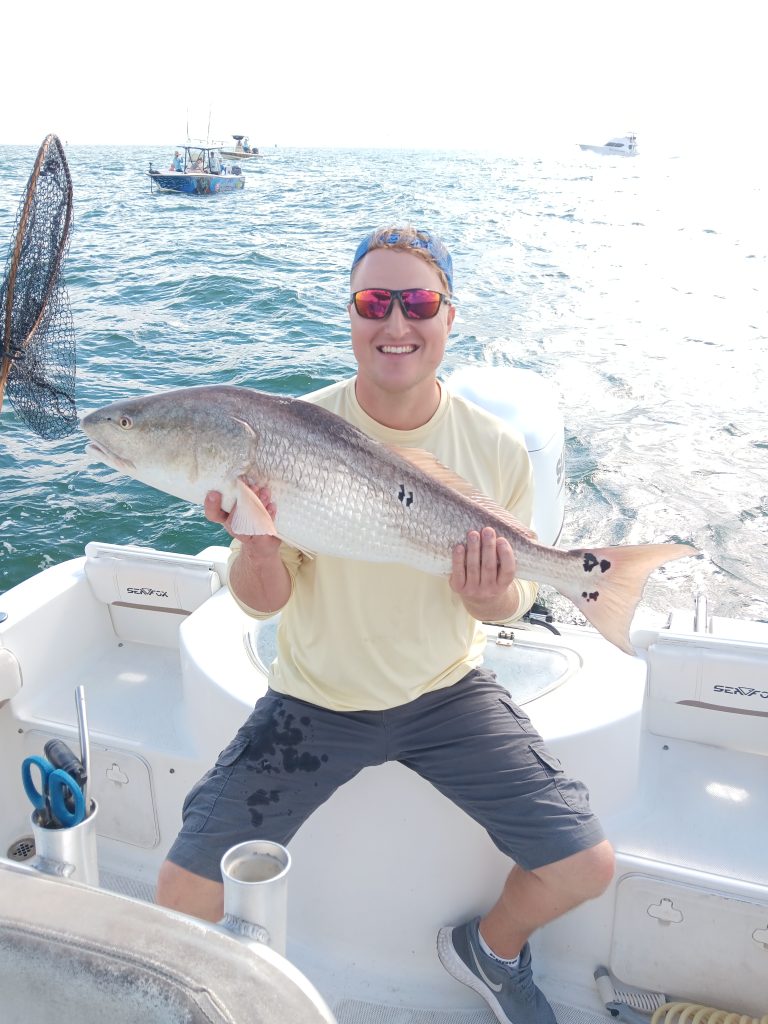 a guy holding a redfish on a boat in new smyrna beach, fl