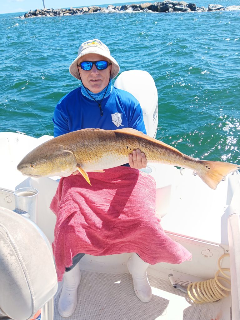 a guy holding a redfish on a boat in new smyrna beach, fl