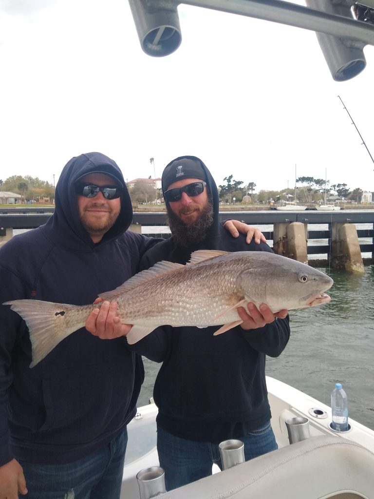 two guys holding a redfish on a boat in new smyrna beach, fl